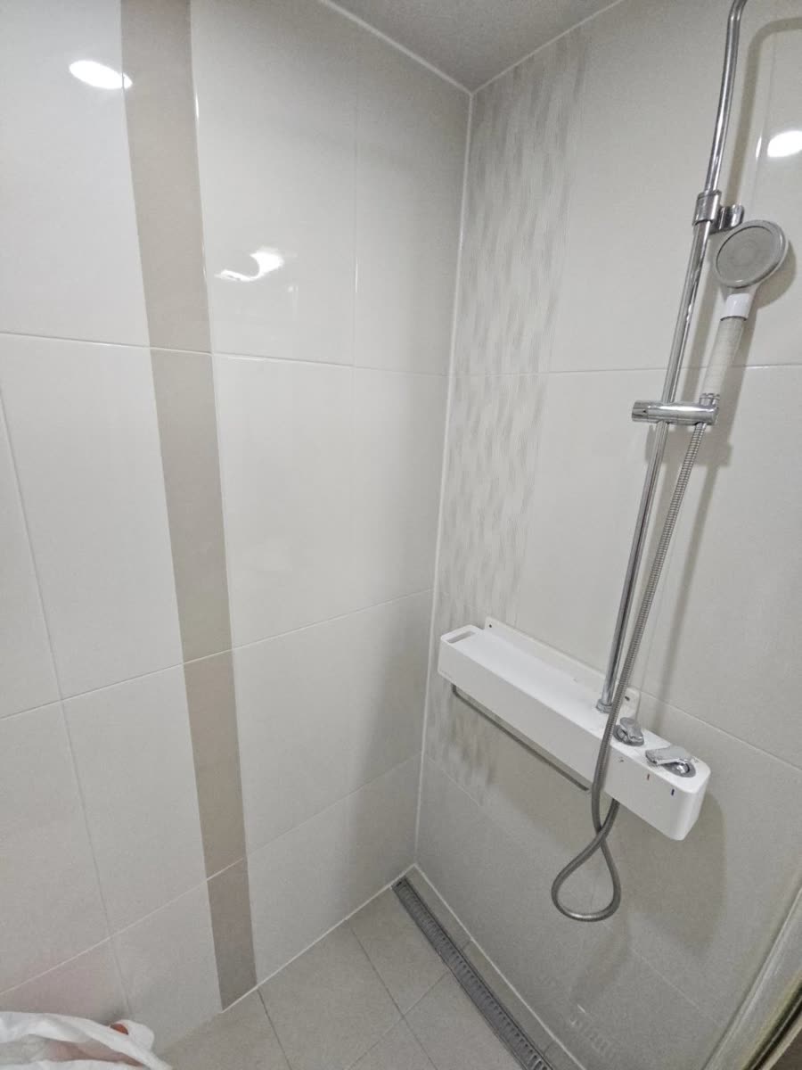 아파트 욕실 샤워 구역 벽면 타일 시공을 마친 흰색 벽과 샤워기