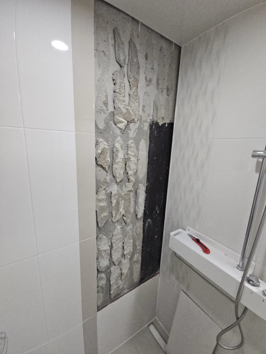 샤워 공간 벽면에서 타일을 떼어내 시멘트 접착 덩어리가 드러난 철거 모습